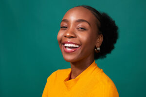 Beautiful Black woman laughing in studio, teal background, fashion lifestyle portrait. High quality photo